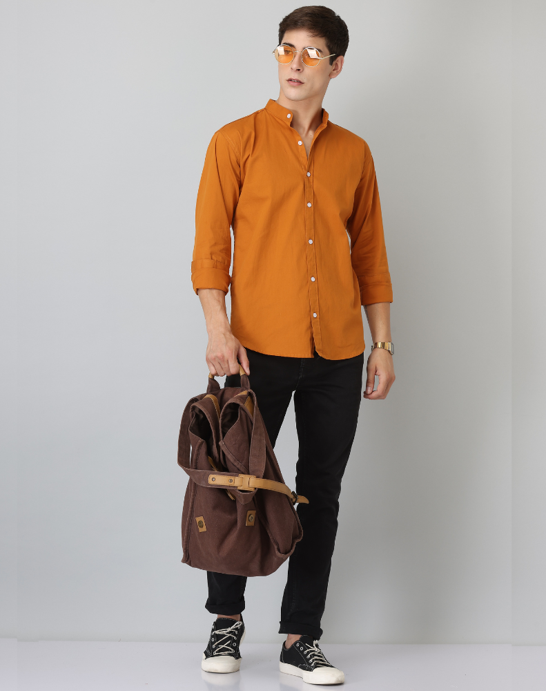 Person wearing an orange shirt and black pants, holding a brown backpack on a plain background