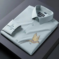 Folded light blue dress shirt with bird embroidery on a dark surface