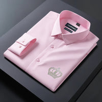 Folded pink dress shirt with a green embroidered logo on a dark surface