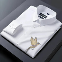 Folded white dress shirt with bird embroidery on a dark surface